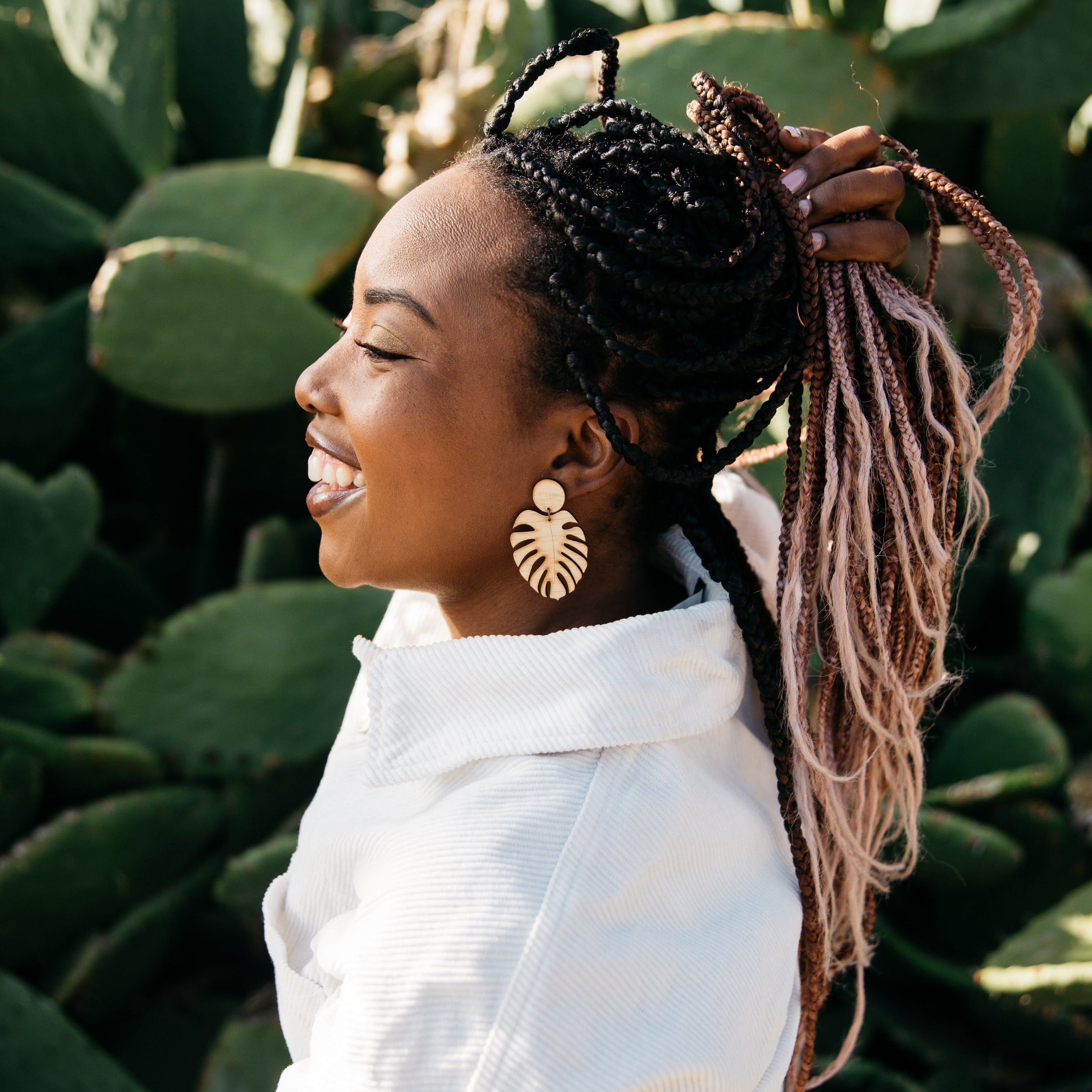 women wearring monstera bamboo earrings, a white jacket behind cactus