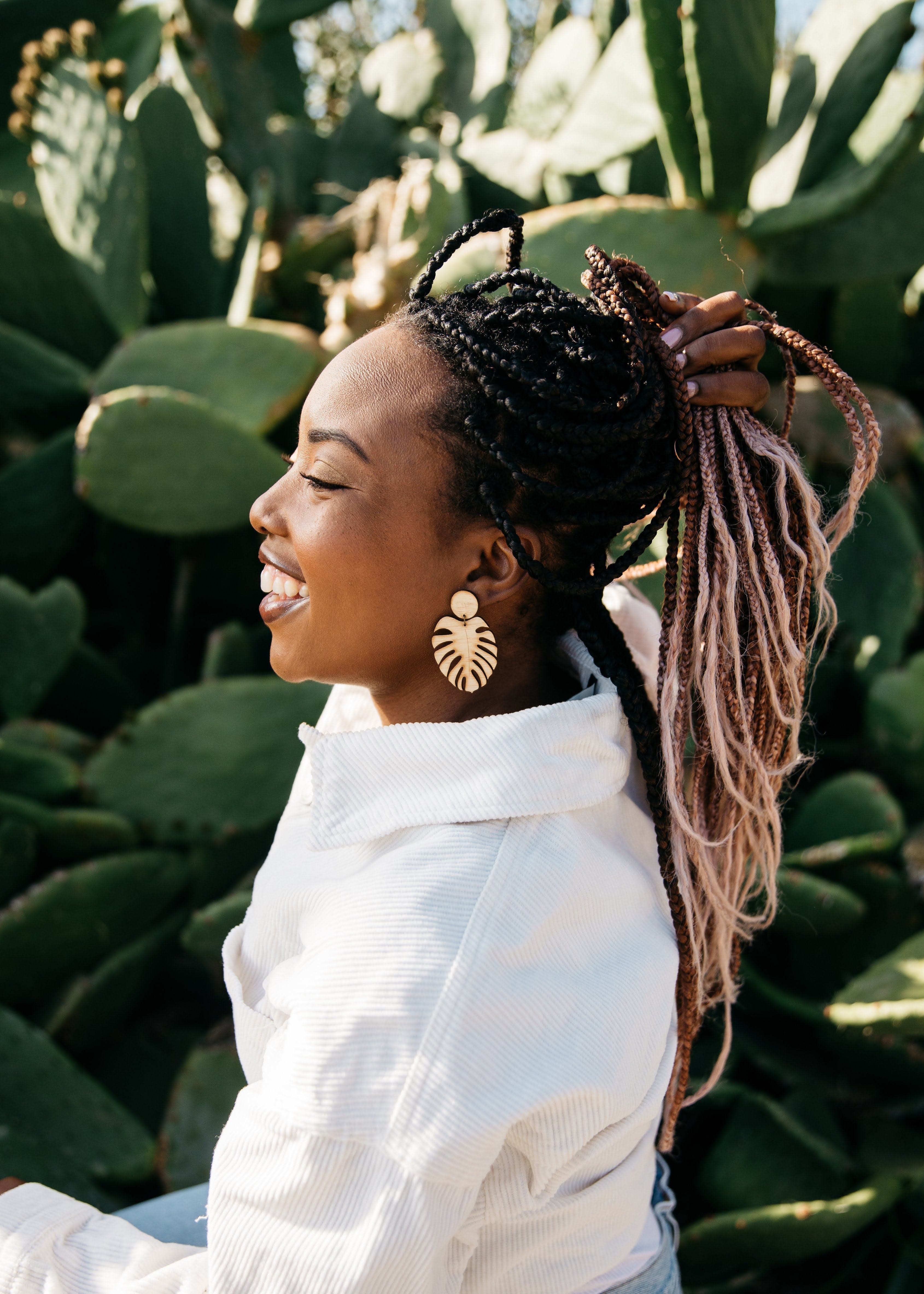 women wearring monstera bamboo earrings, a white jacket behind cactus