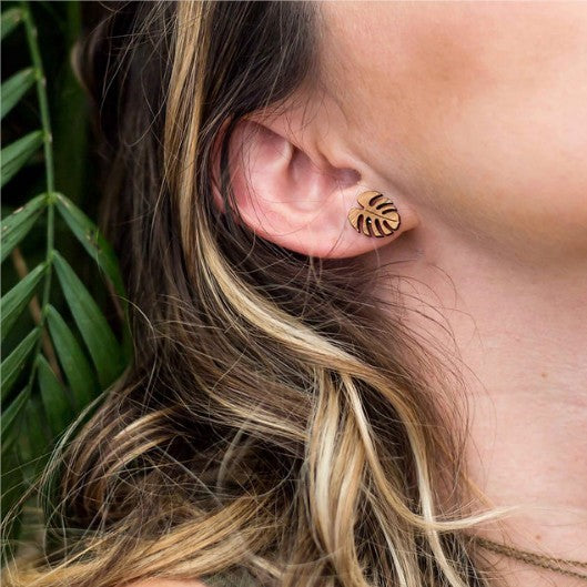 a women wearing sustianable bamboo monstera earrings leaning on a tropical leaf