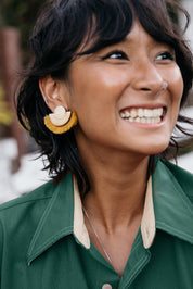 Woman wearing a mustard fringe and wood earrings and green shirt with a blurred natural background