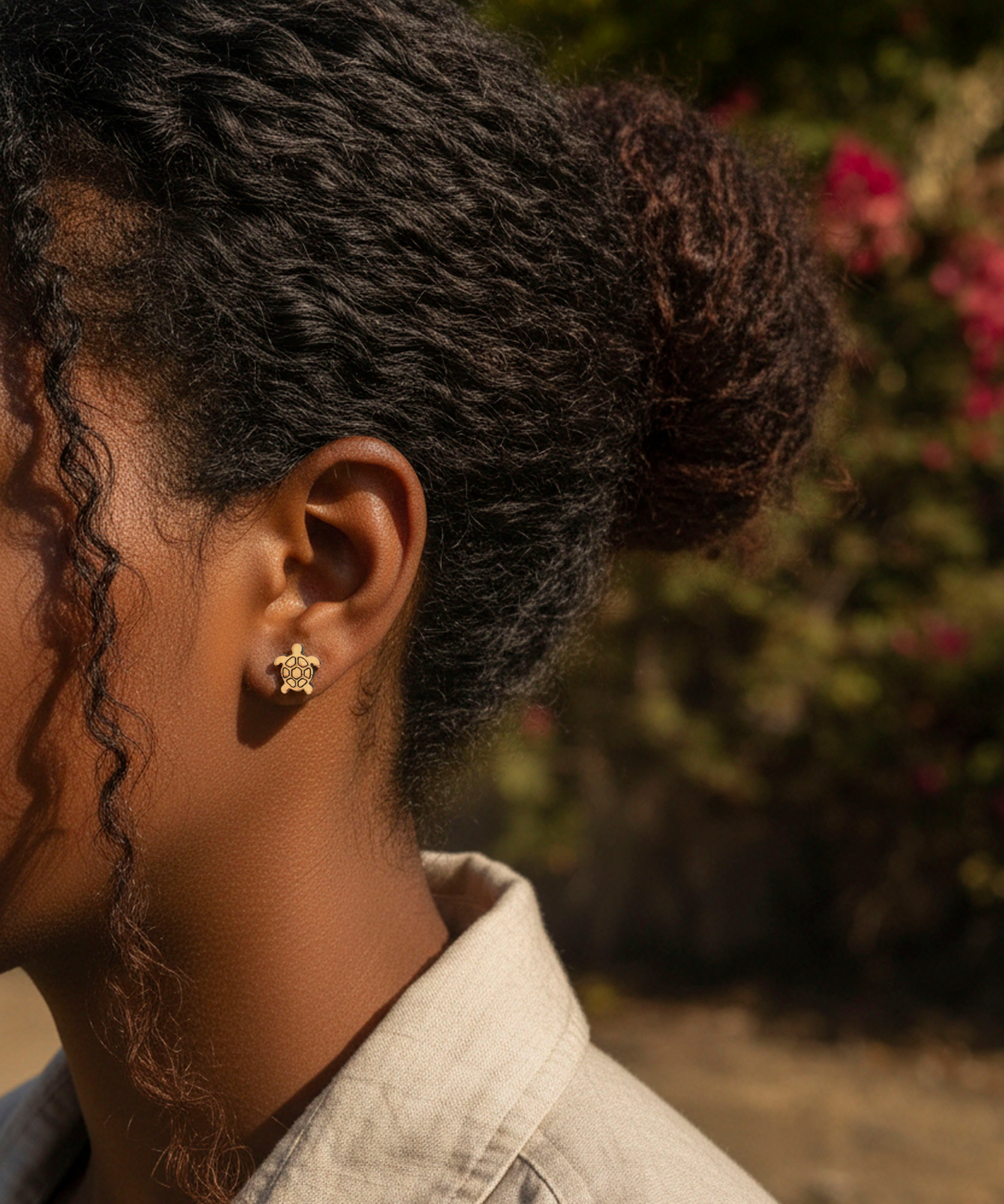 Person with styled hair wearing cute tortoise stud wood earrings, standing outdoors with blurred background