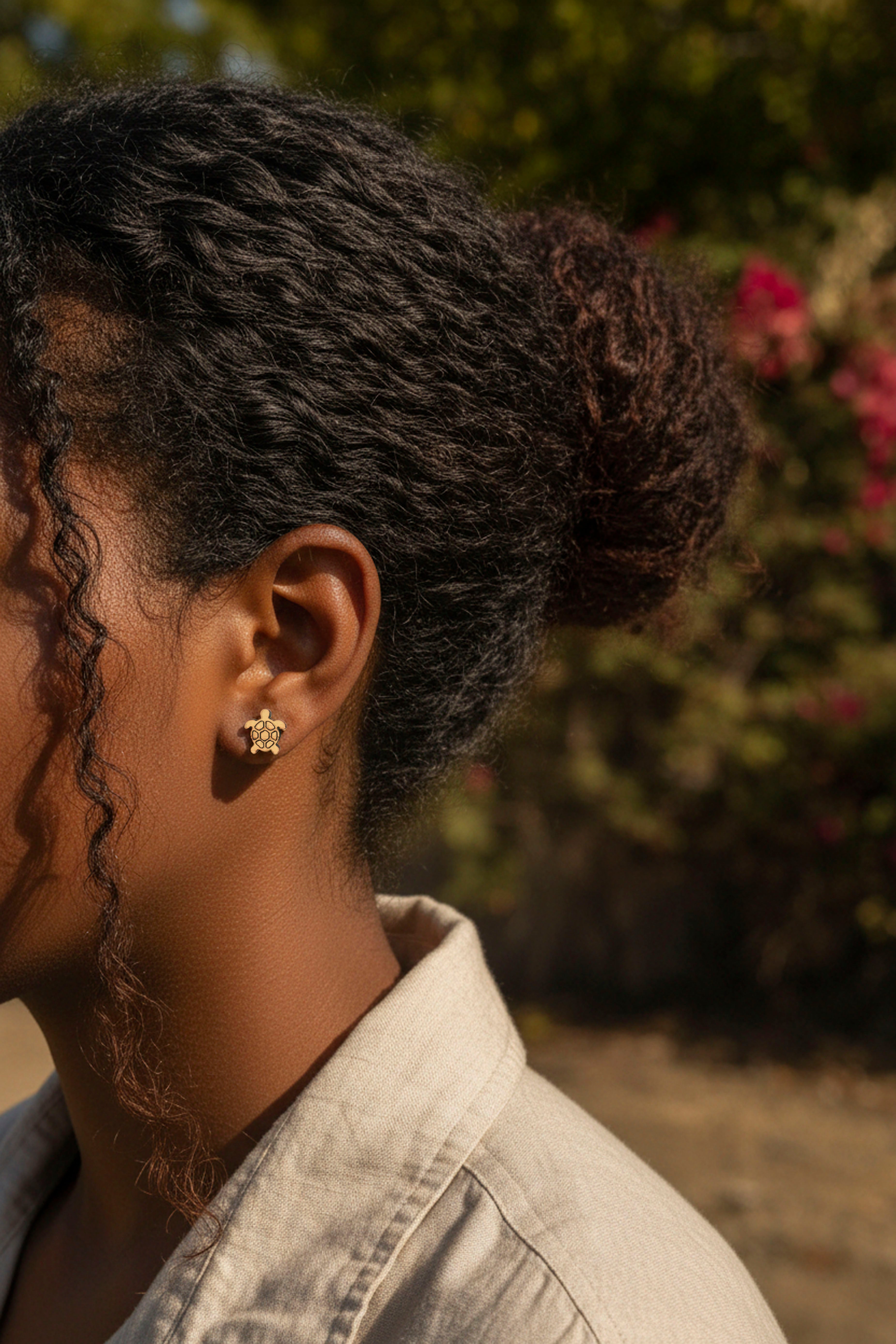 Person with styled hair wearing cute tortoise stud wood earrings, standing outdoors with blurred background