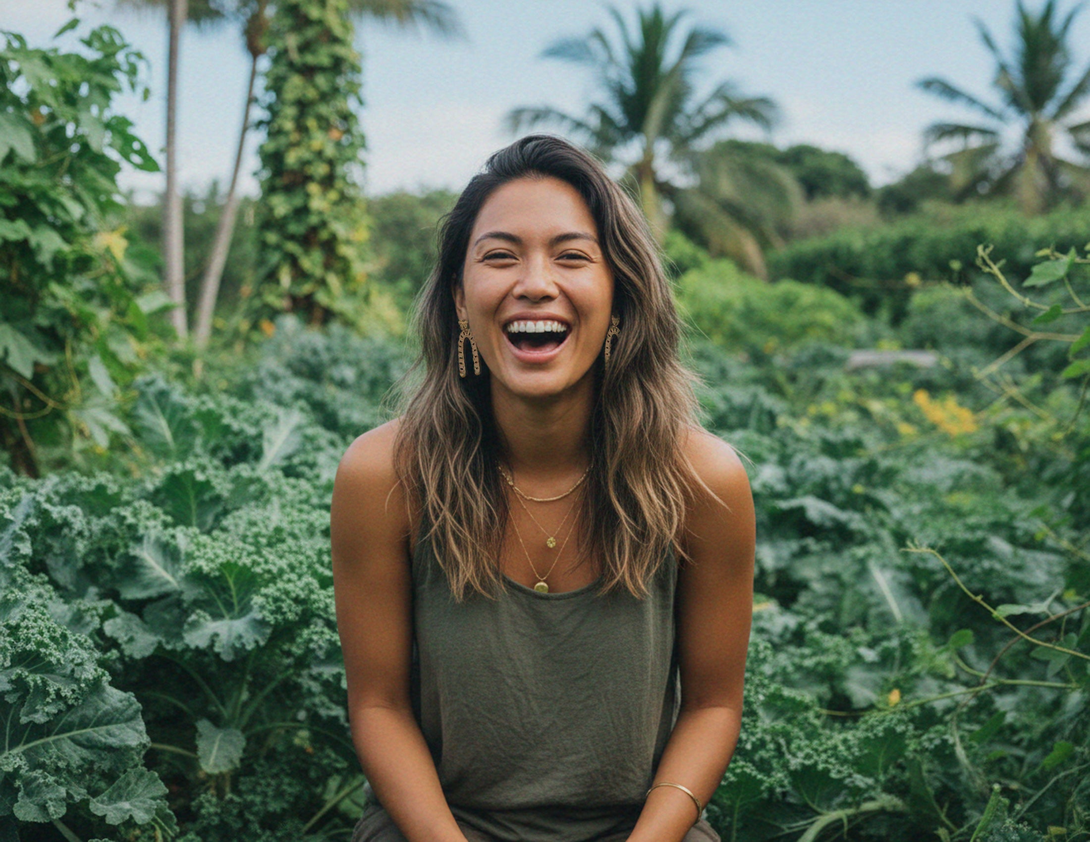 Woman laughing wearing arch bamboo drop earring in a lush green garden with palm trees in the background