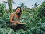 Woman wearing ethically made u shape arch bamboo earrings in a garden holding kale, surrounded by greenery