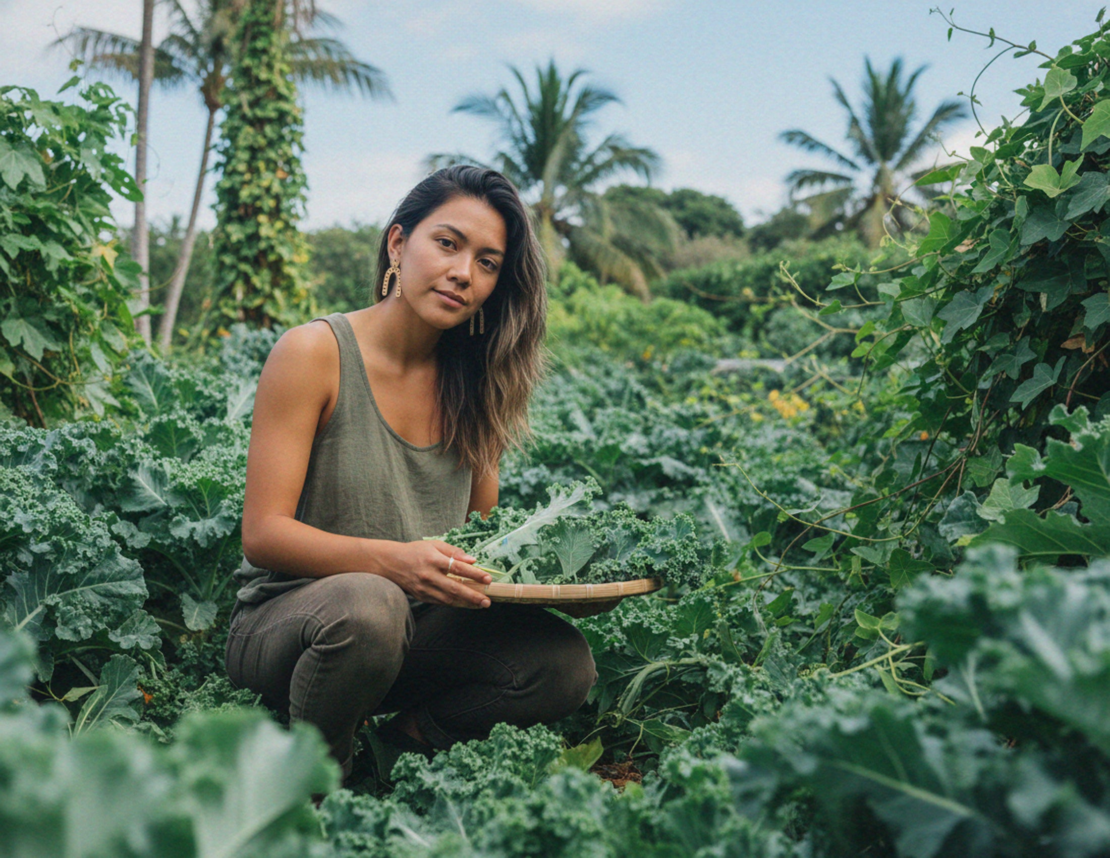 Woman wearing ethically made u shape arch bamboo earrings in a garden holding kale, surrounded by greenery