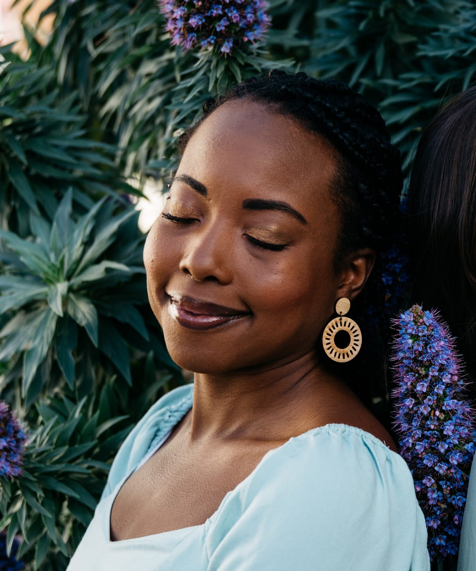Woman with large Relaia bamboo circle earrings standing in front of a plant with purple flowers