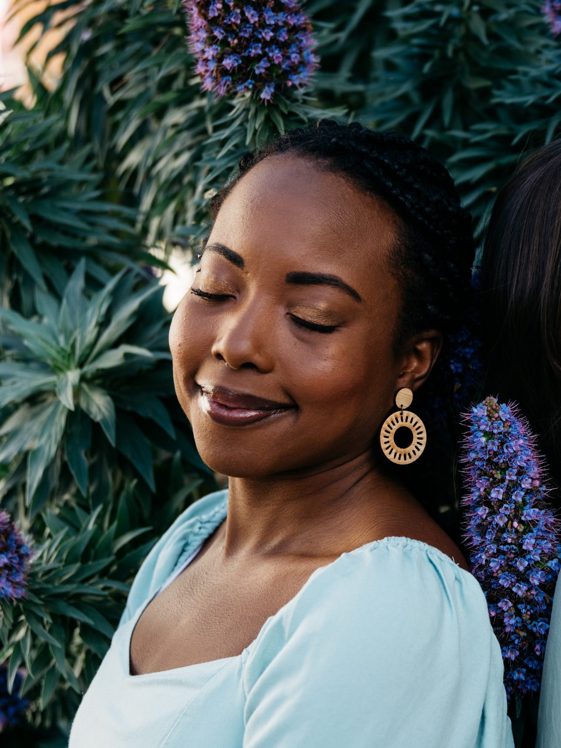 Woman with large Relaia bamboo circle earrings standing in front of a plant with purple flowers