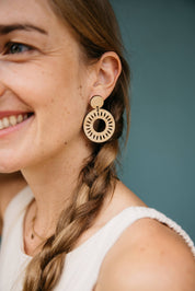 Close-up of a woman wearing circle laser-cut-drop earrings with a braided hairstyle against a blue background