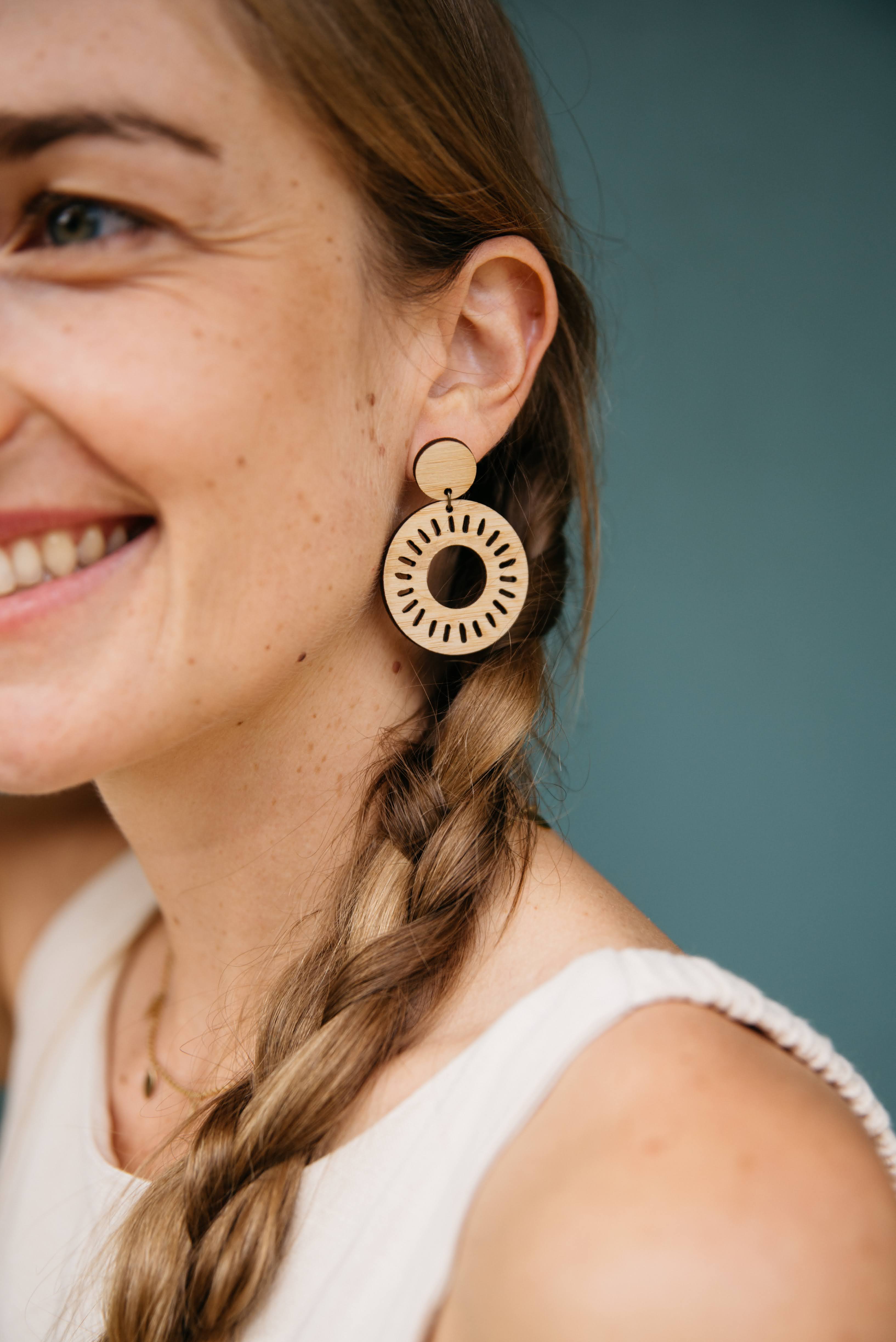 Close-up of a woman wearing circle laser-cut-drop earrings with a braided hairstyle against a blue background