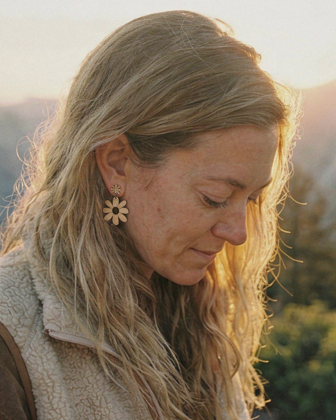 Woman wearing a daisy earring outdoors with a blurred natural background