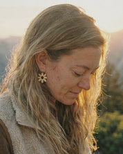 Woman wearing a daisy earring outdoors with a blurred natural background
