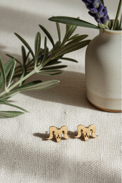 wood bighorn sheep shaped earrings on a textured surface with a vase of lavender in the background.