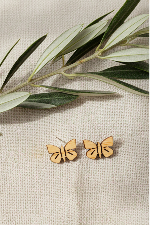 Wooden butterfly earrings on a beige fabric background with green leaves.