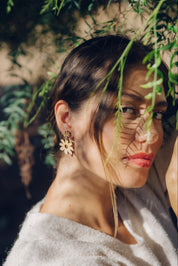 Woman with daisy dangle earrings standing among green foliage
