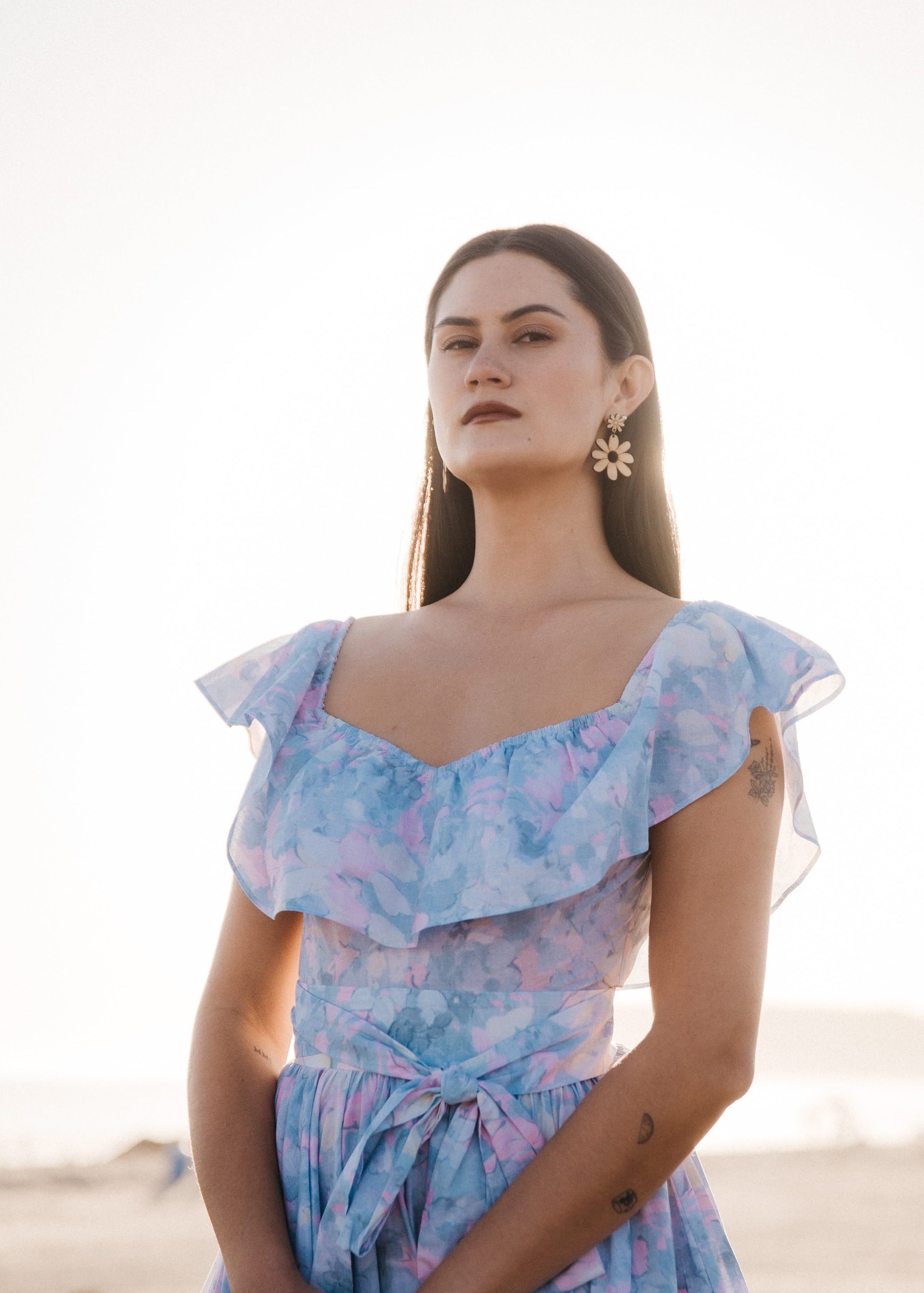 Woman wearing large statement daisy earrings with a light blue floral dress with a blurred background