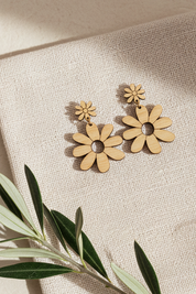 Wooden daisy-shaped earrings on a beige fabric background with a branch.