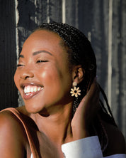 Woman with braided hair wearing a daisy earring against a textured wall.