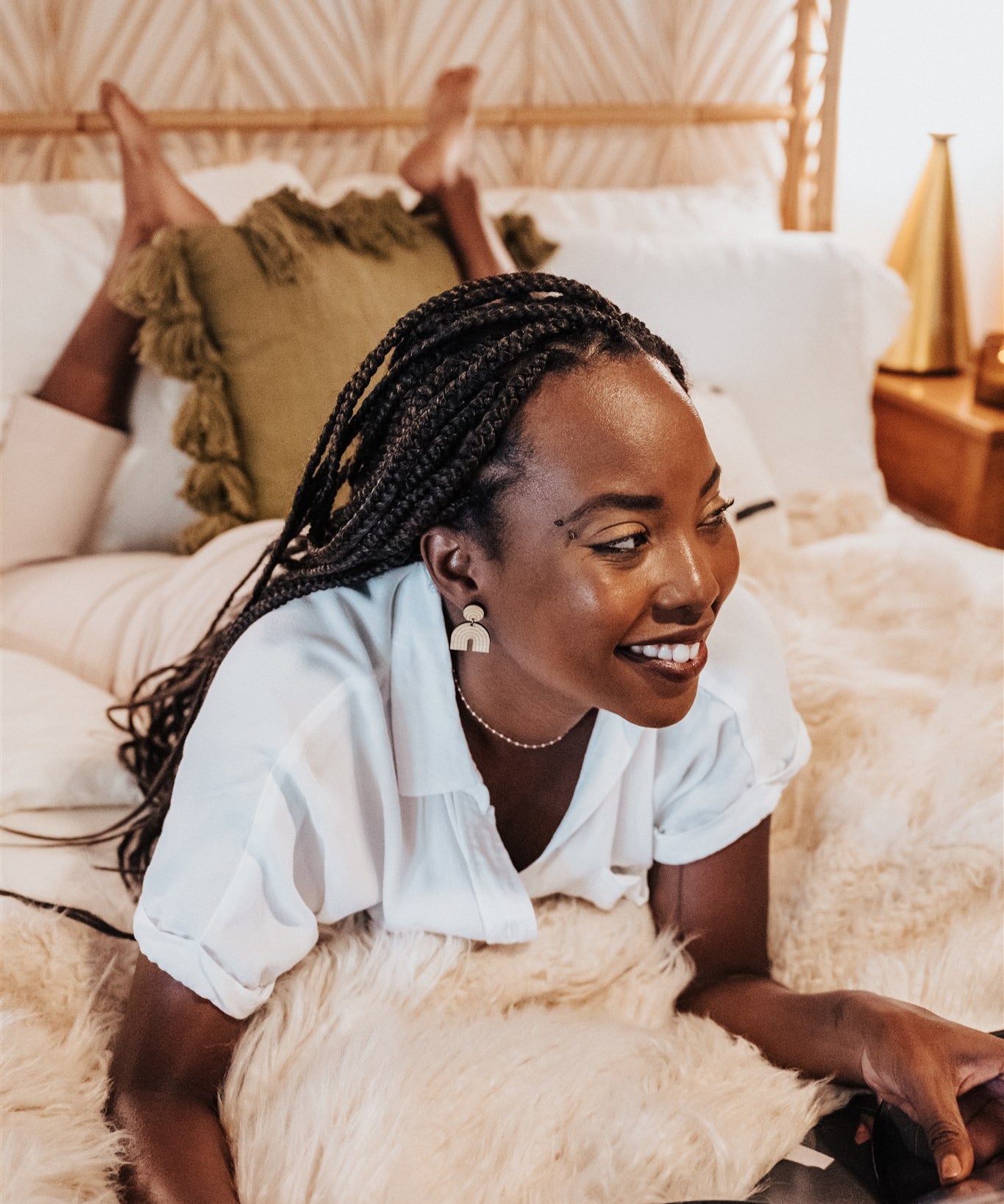 Woman wearing simple rainbow dangle wood earrings, laying on a bed in a cozy room.