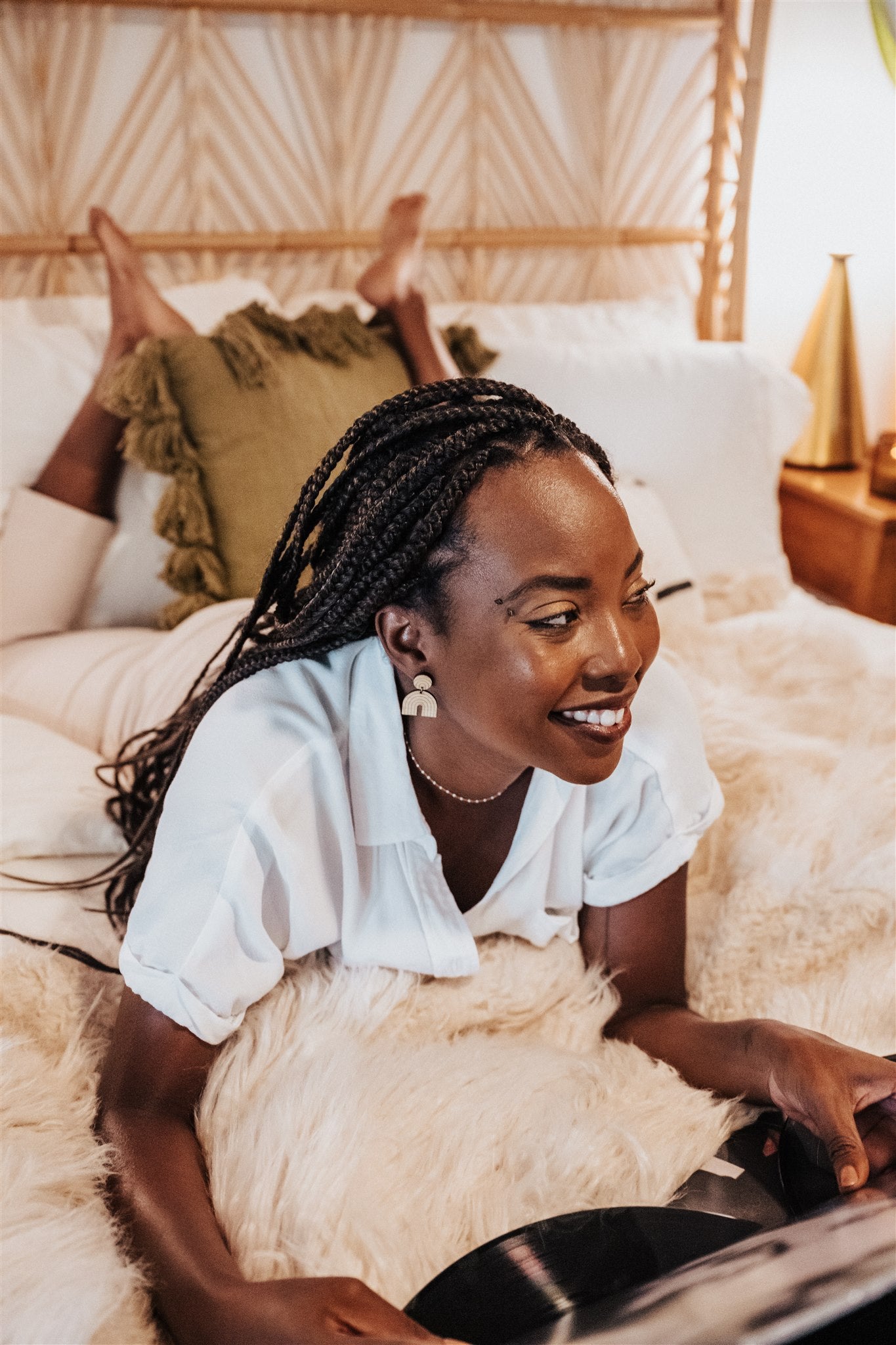 Woman wearing simple rainbow dangle wood earrings, laying on a bed in a cozy room.
