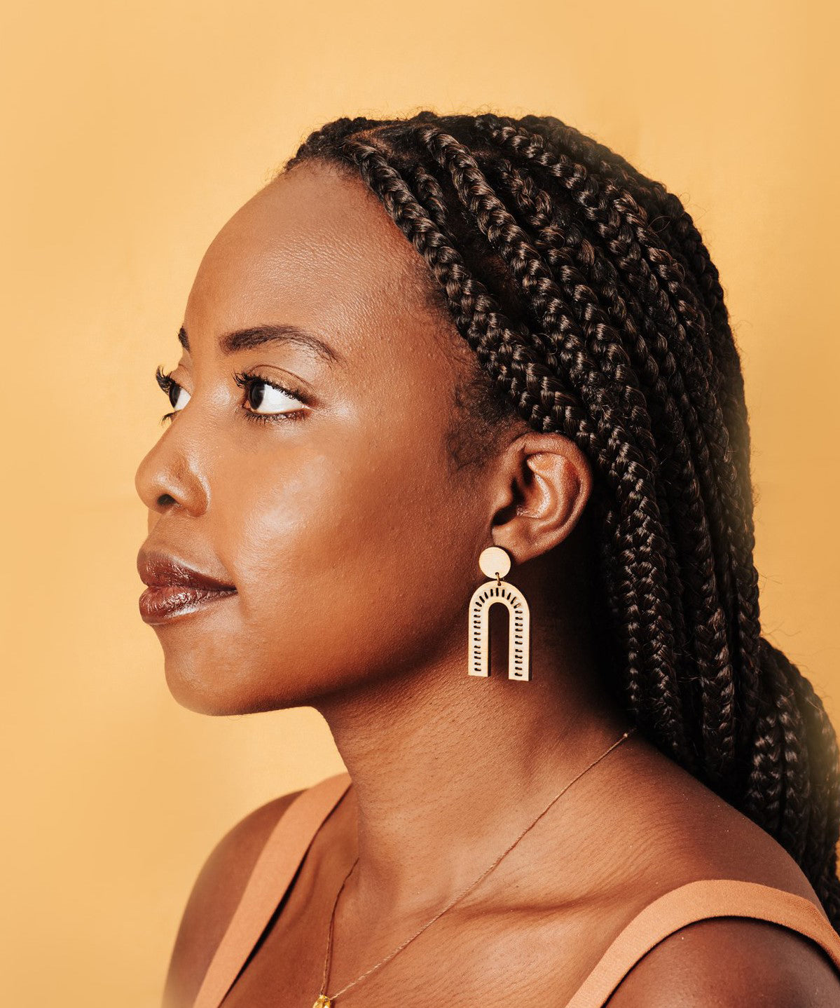 Woman with braided hair wearing delicate arch earrings against a beige background