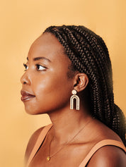 Woman with braided hair wearing delicate arch earrings against a beige background