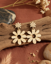 Floral earrings on a rustic background with wood, stones, and dried plants.