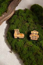 Wooden boot and backpack stud earrings on a patch of green moss.