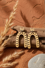 bamboo horseshoe earrings on a wooden log with wheat and a stone on a brown background
