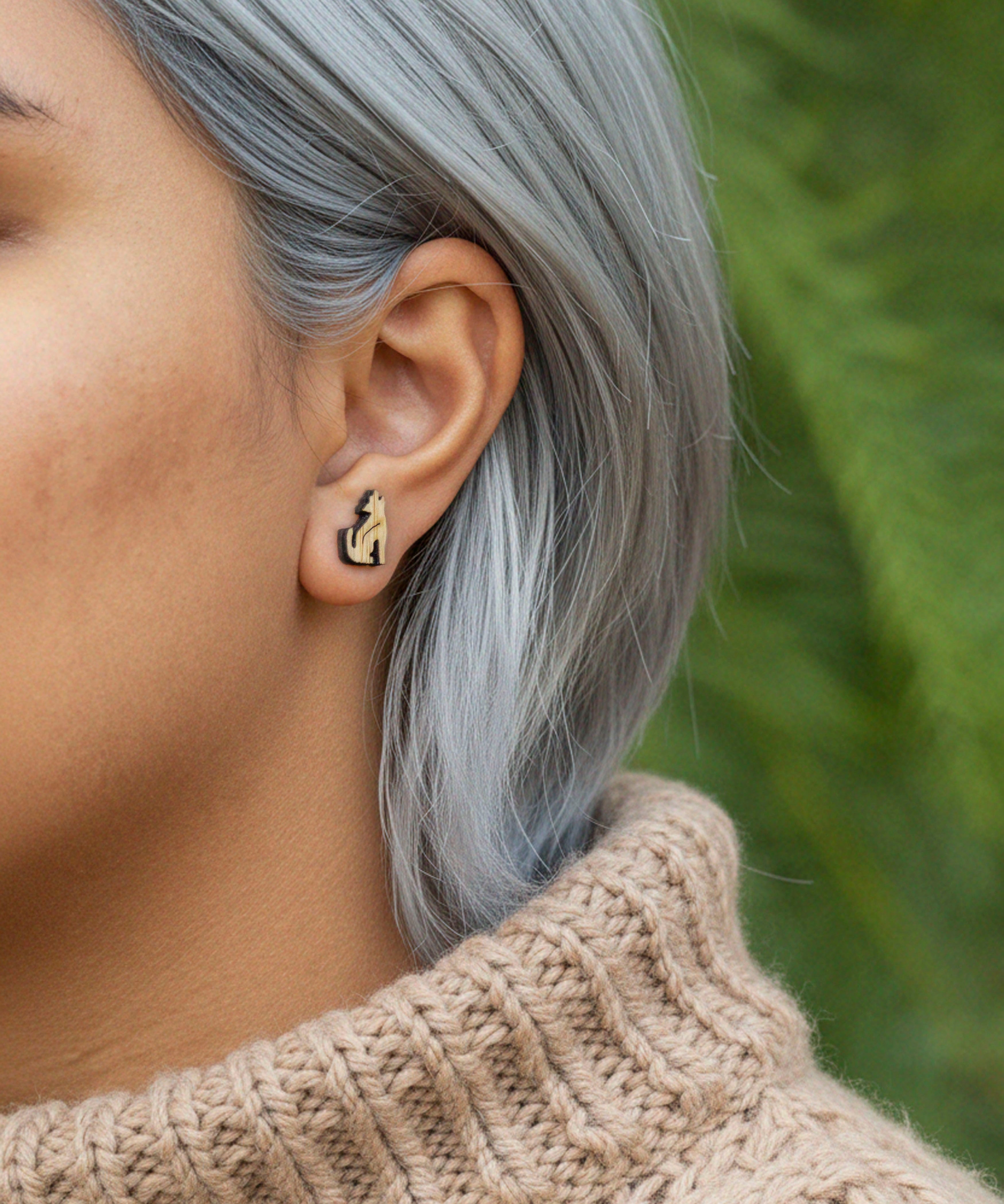 Close-up of a person wearing a howling coyote bamboo hypoallergenic earring with a blurred green background