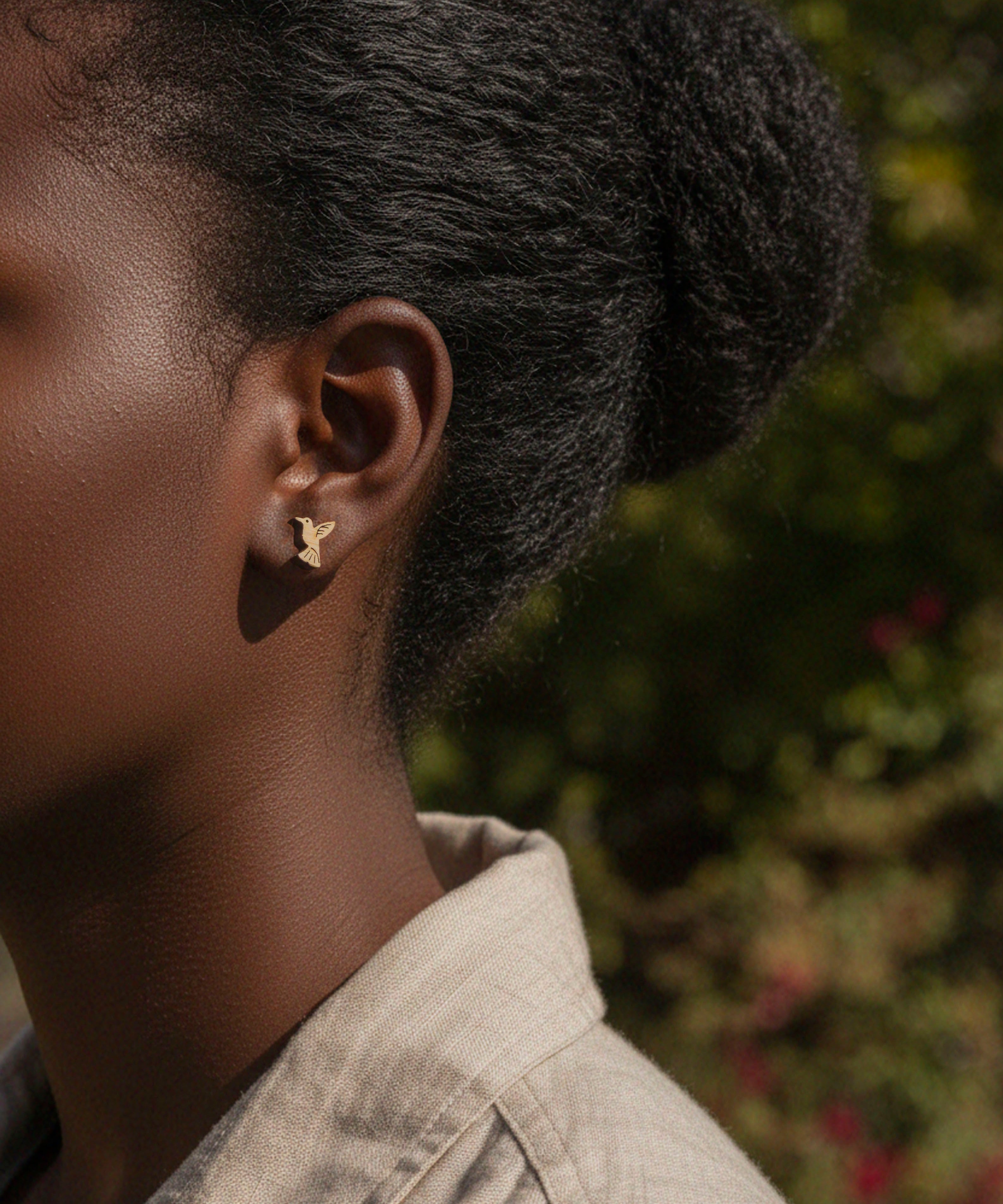 Close-up of a person wearing a cute hummingbird stud wood earring with a blurred natural background