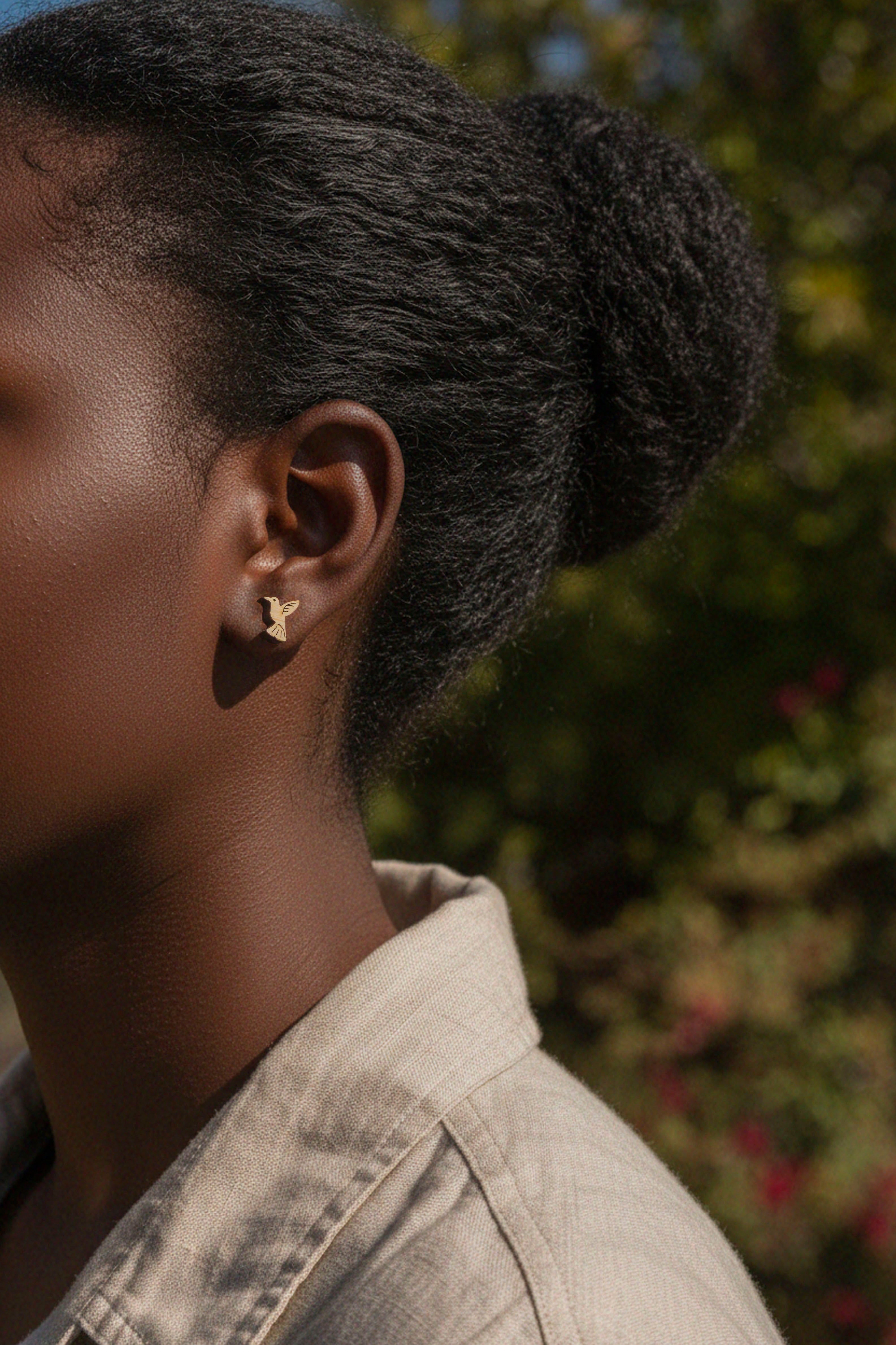Close-up of a person wearing a cute hummingbird stud wood earring with a blurred natural background