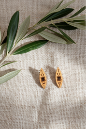 Wooden kayak-shaped stud earrings on a textured beige surface with olive leaves.