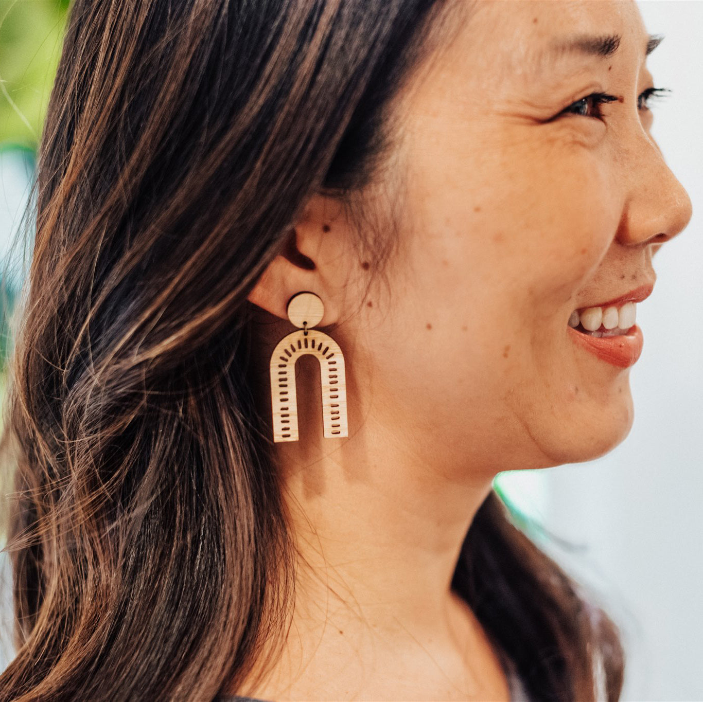 Close-up of a woman wearing laser-cut arch bamboo earrings with a blurred background