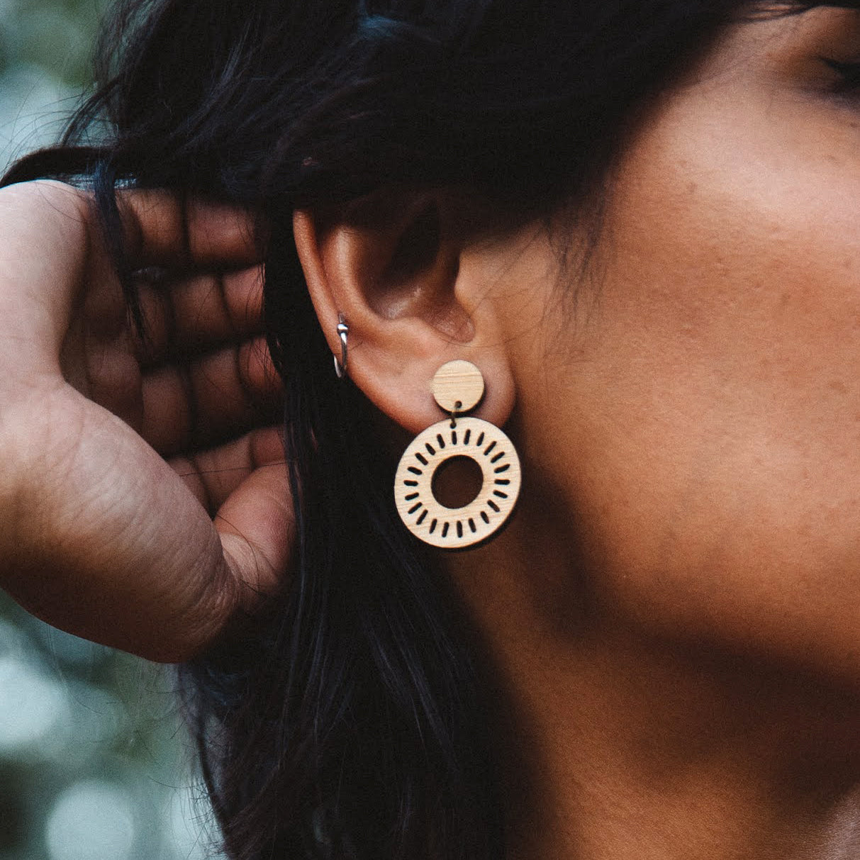 Close-up of a person wearing laser cut wood dangle earring with a blurred background. Perfect for everyday wear
