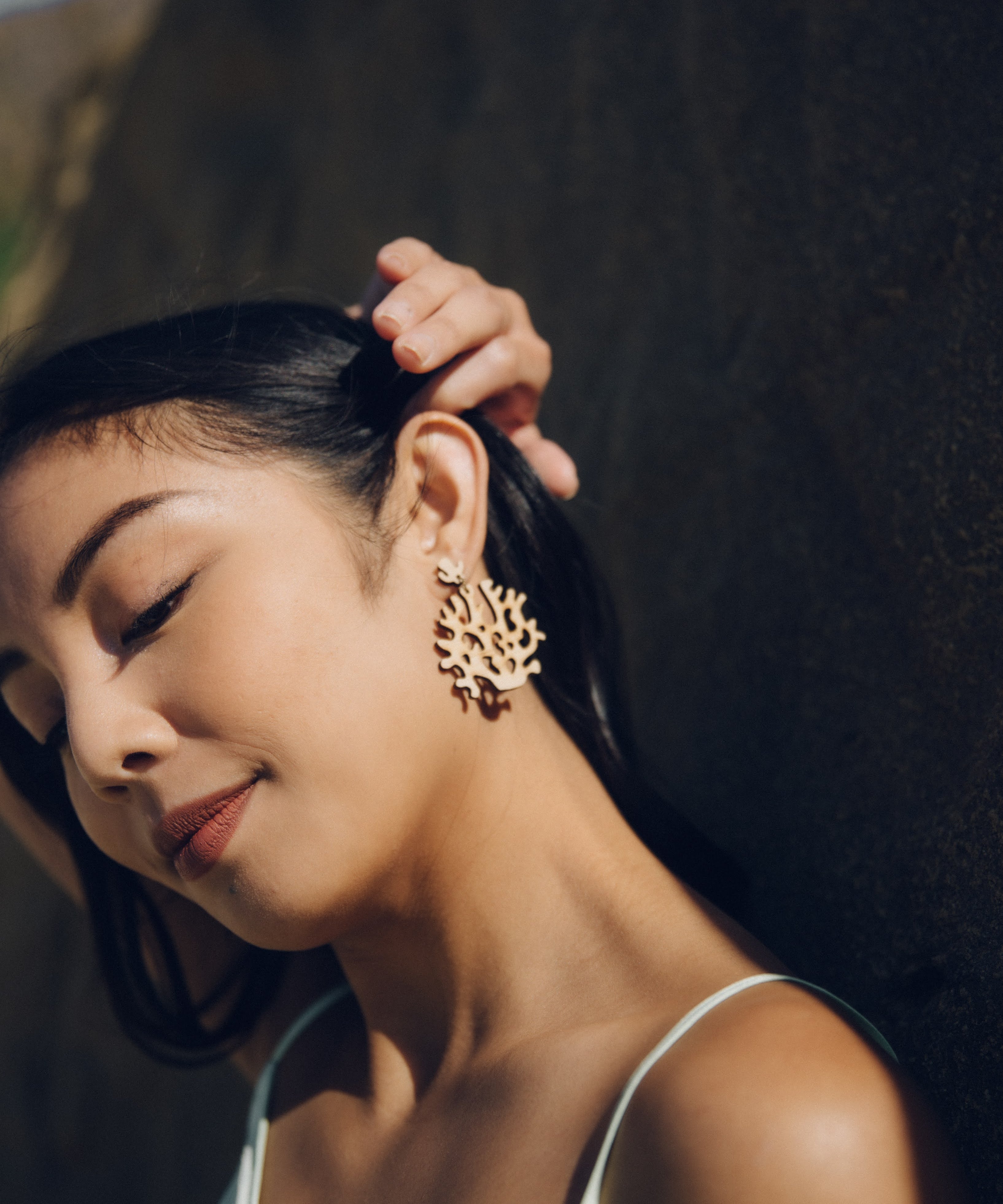 Woman wearing lightweight coral wood earrings on beach with a blurred background