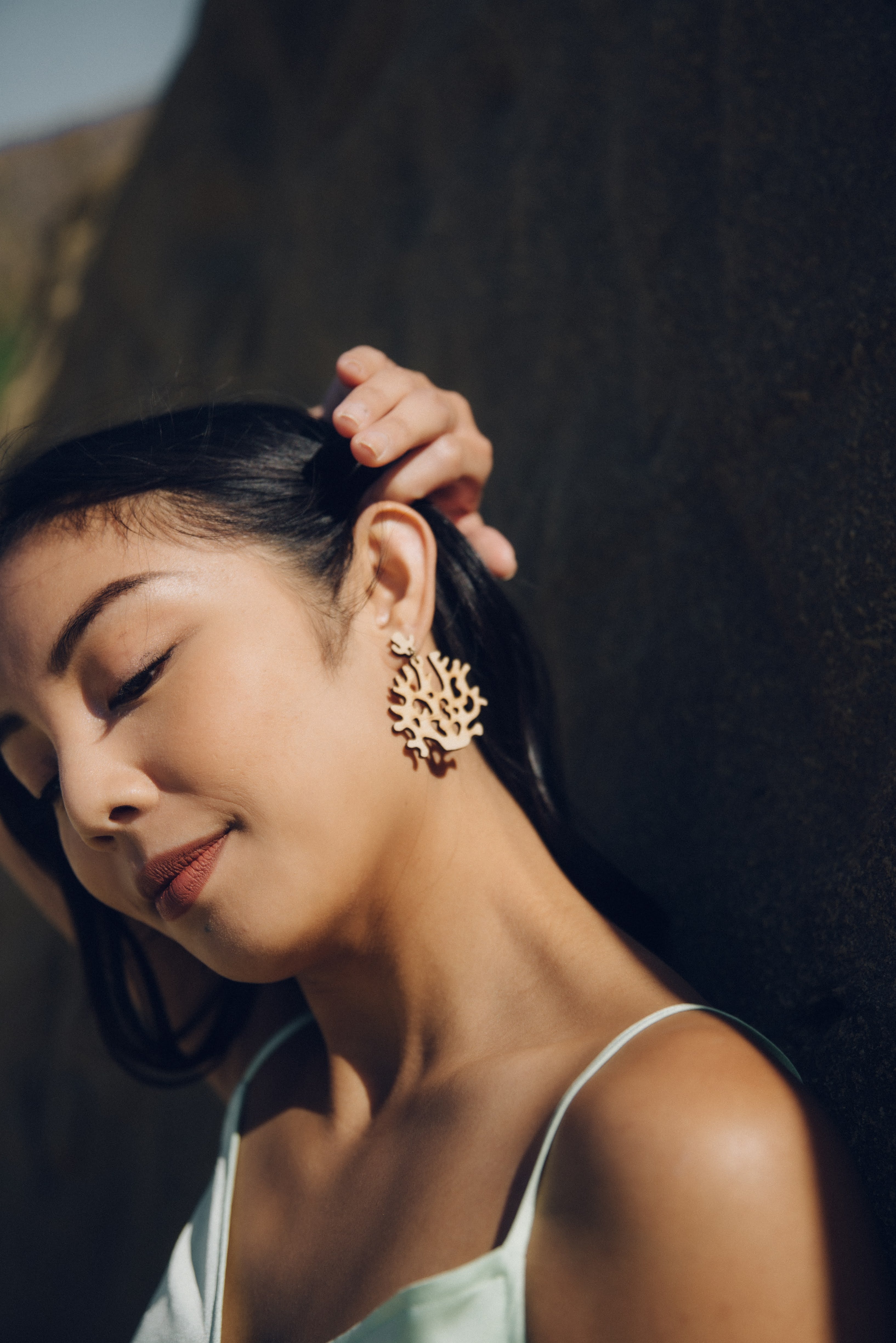 Woman wearing lightweight coral wood earrings on beach with a blurred background