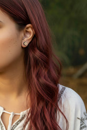 Close-up of a person with wavy red hair wearing maple leaf - Canada's emblem  earrings outdoors.