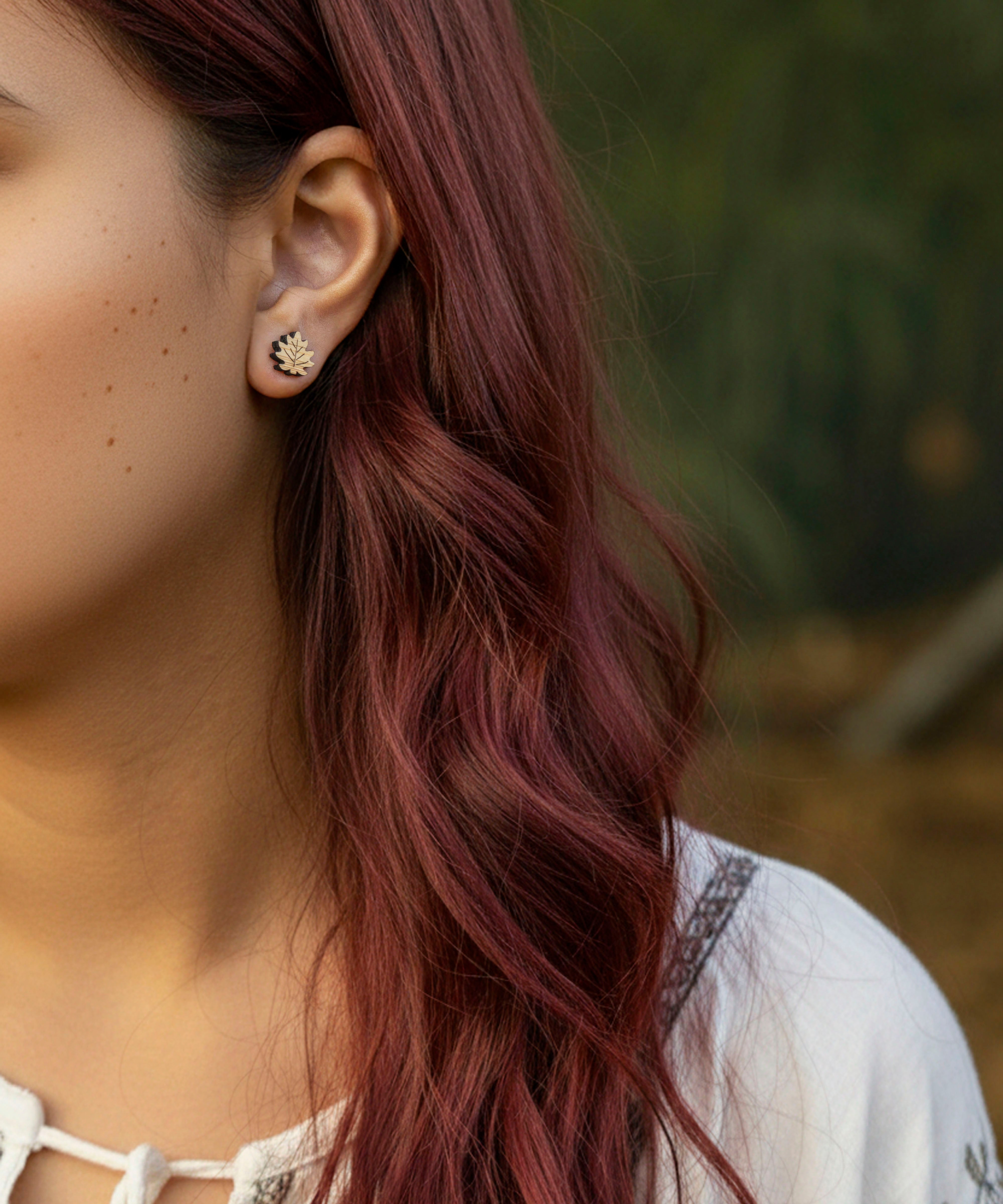 Close-up of a person with wavy red hair wearing maple leaf - Canada's emblem  earrings outdoors.