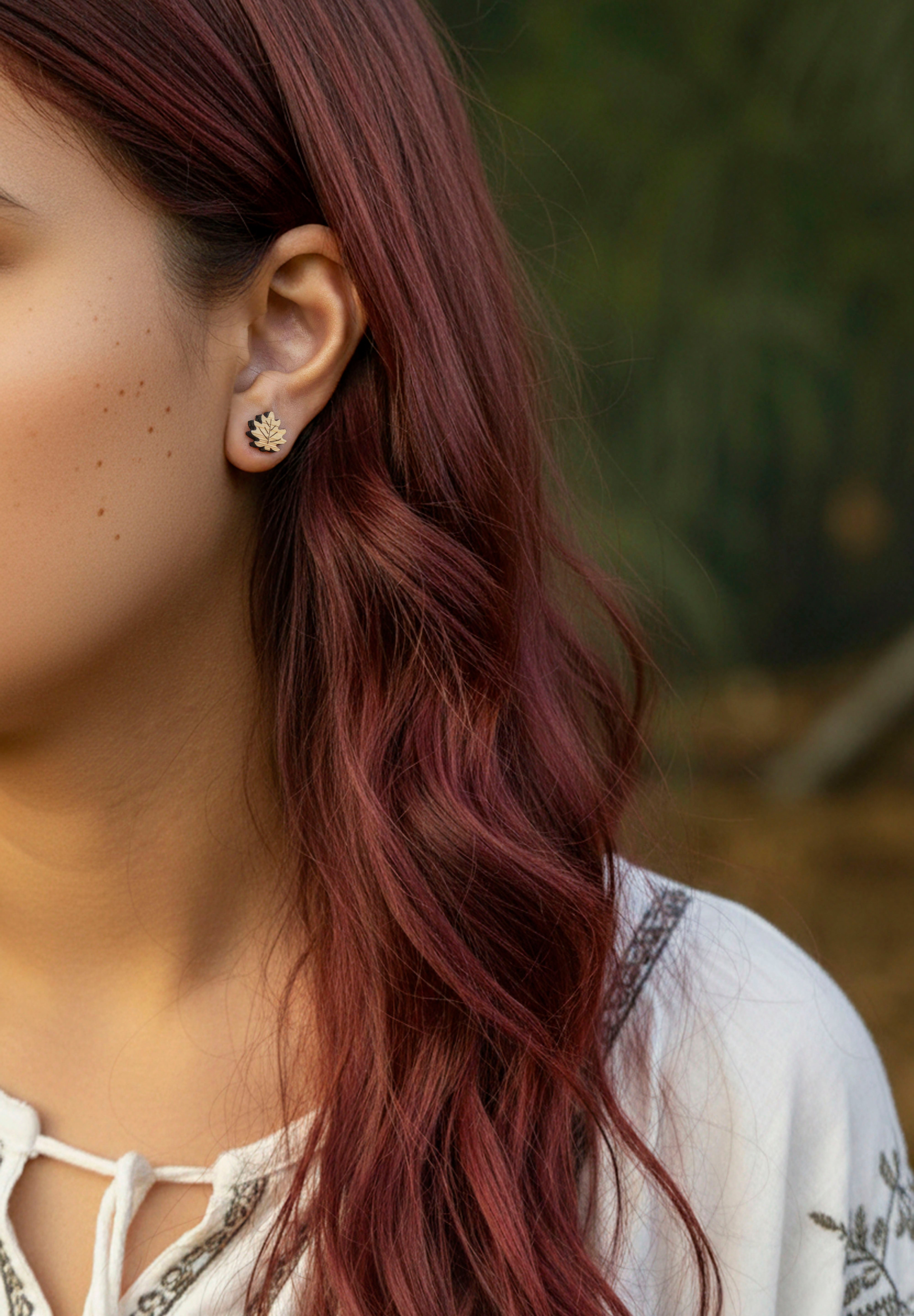 Close-up of a person with wavy red hair wearing maple leaf - Canada's emblem  earrings outdoors.
