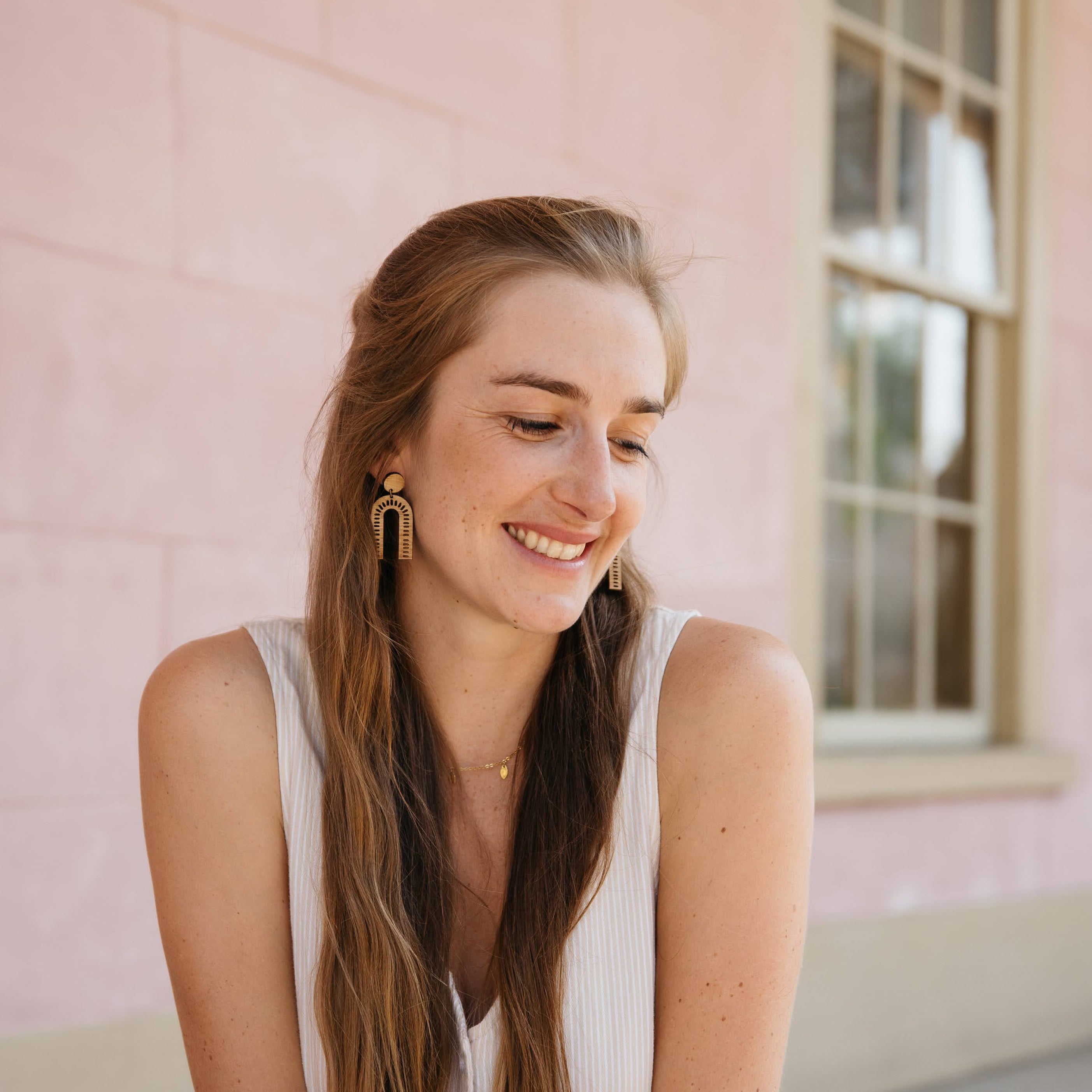 Woman wearing minimalist arch wooden earrings against a pink wall