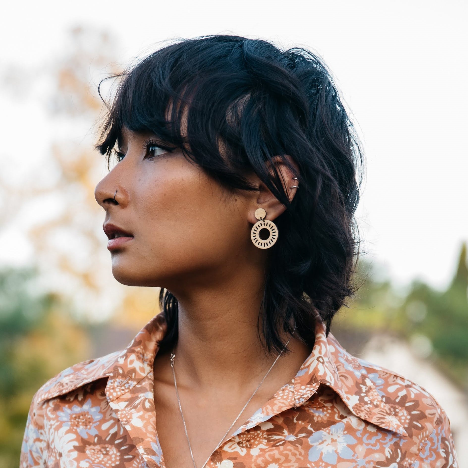 Woman with short dark hair wearing minimalist drop wooden earrings and a floral shirt outdoors. Perfect gift for your environmentally conscious friends.
