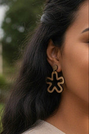 Close-up of a person wearing minimalist flower cutout dangle earring with a blurred outdoor background