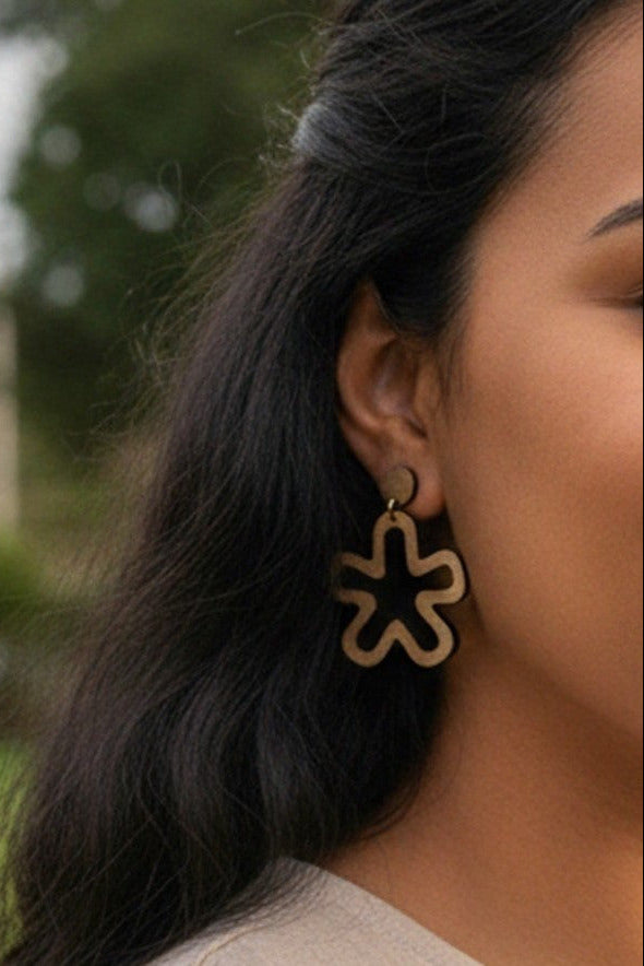 Close-up of a person wearing minimalist flower cutout dangle earring with a blurred outdoor background