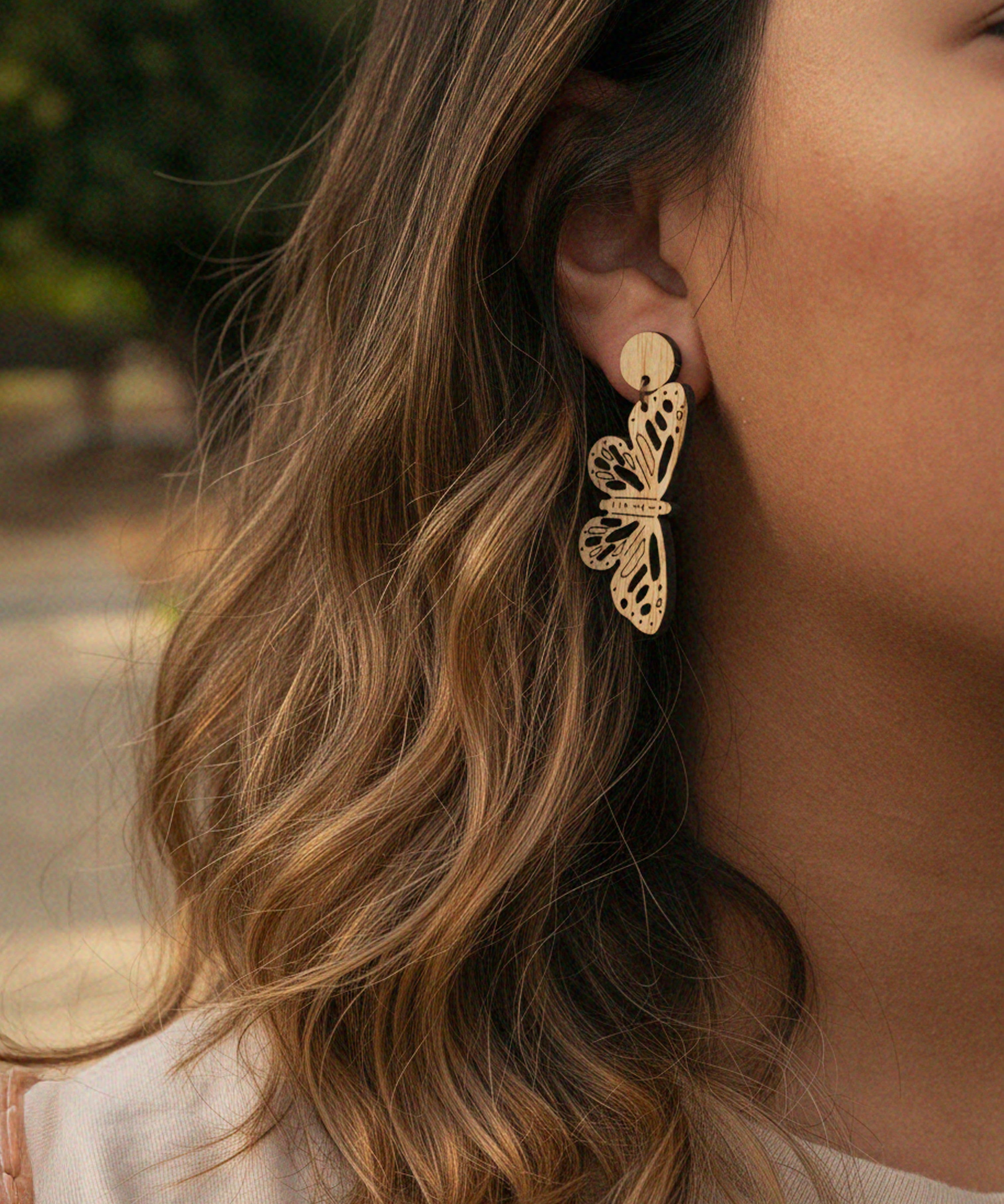 Close-up of a person wearing laser cut butterfly dangle earrings with blurred background