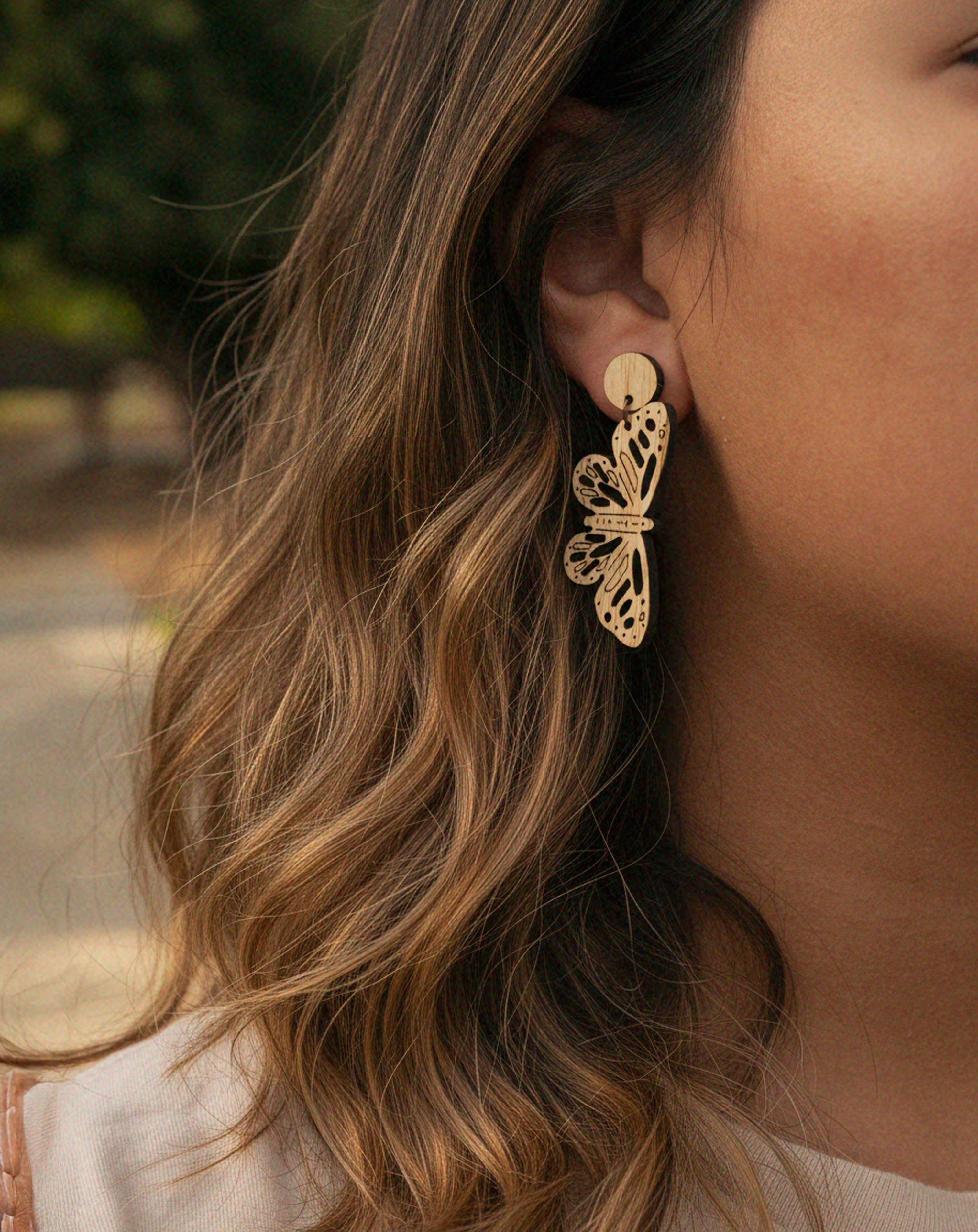 Close-up of a person wearing laser cut butterfly dangle earrings with blurred background
