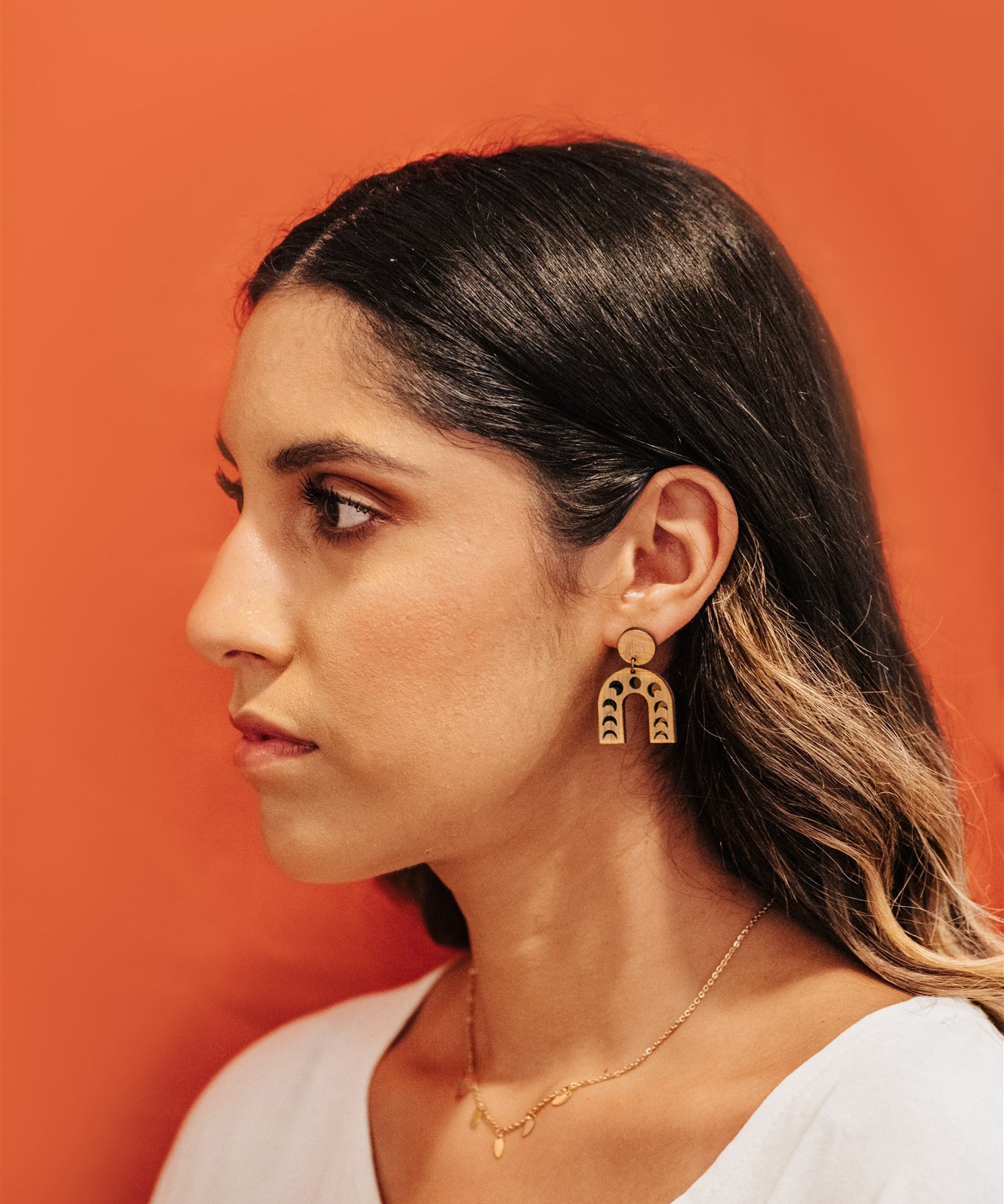 Woman wearing moon-phases arch drop wooden earrings against an orange background