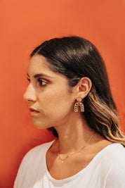 Woman wearing moon-phases arch drop wooden earrings against an orange background