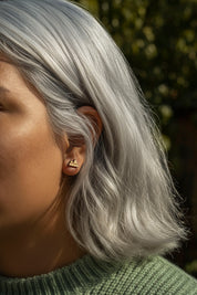 Close-up of a person with silver hair wearing mountain stud earring, with a blurred natural background.