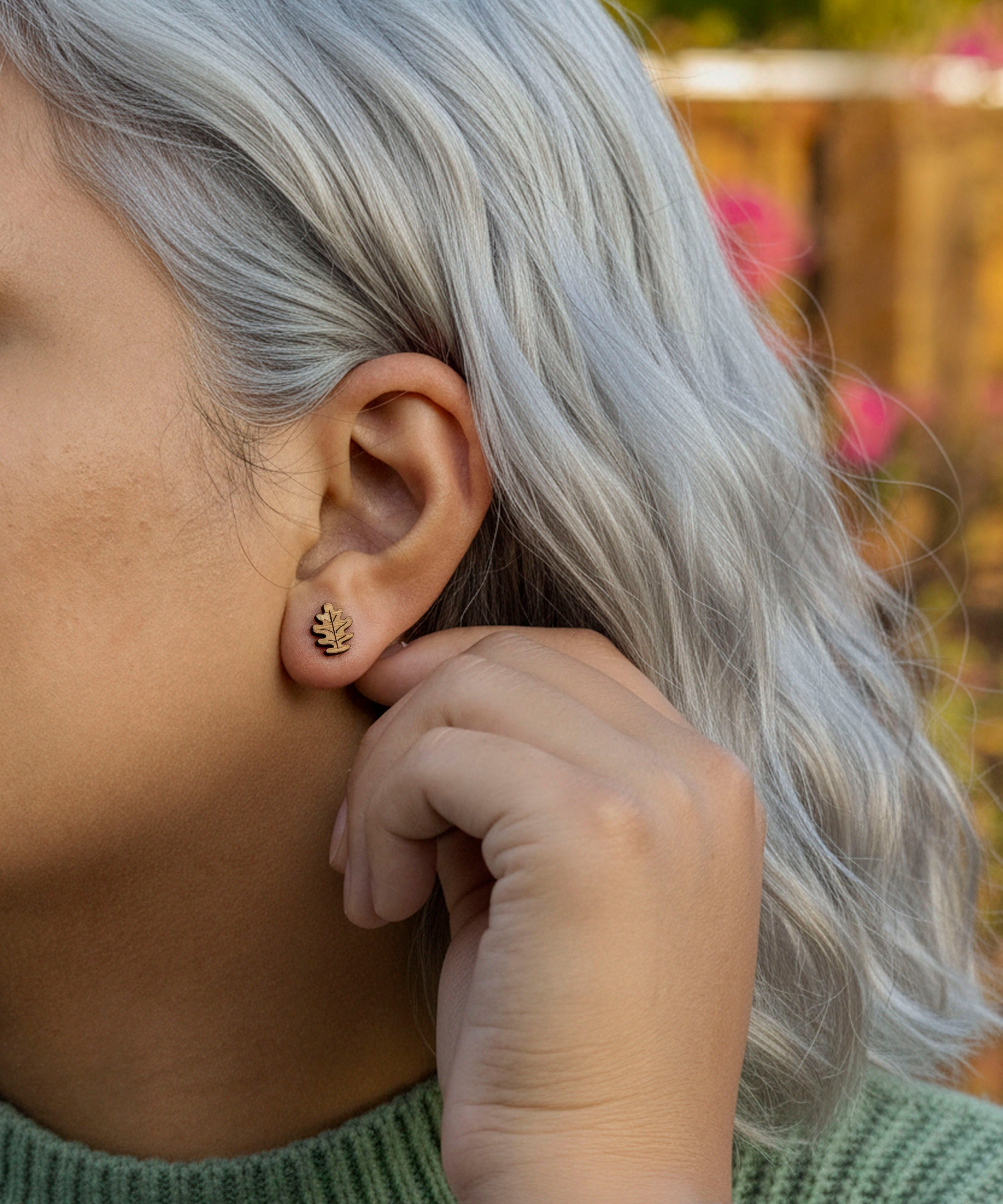 Person with silver hair wearing a small oak leaf earring outdoors