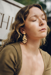 Woman wearing paintbrush flower dangle earrings with a blurred background